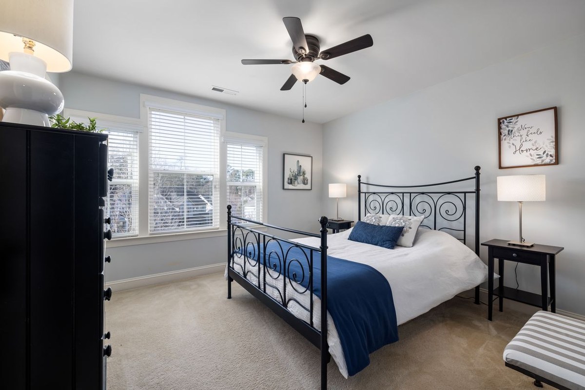Bedroom with a black metal scrollwork bed frame, white duvet, and navy throw beside matching nightstands