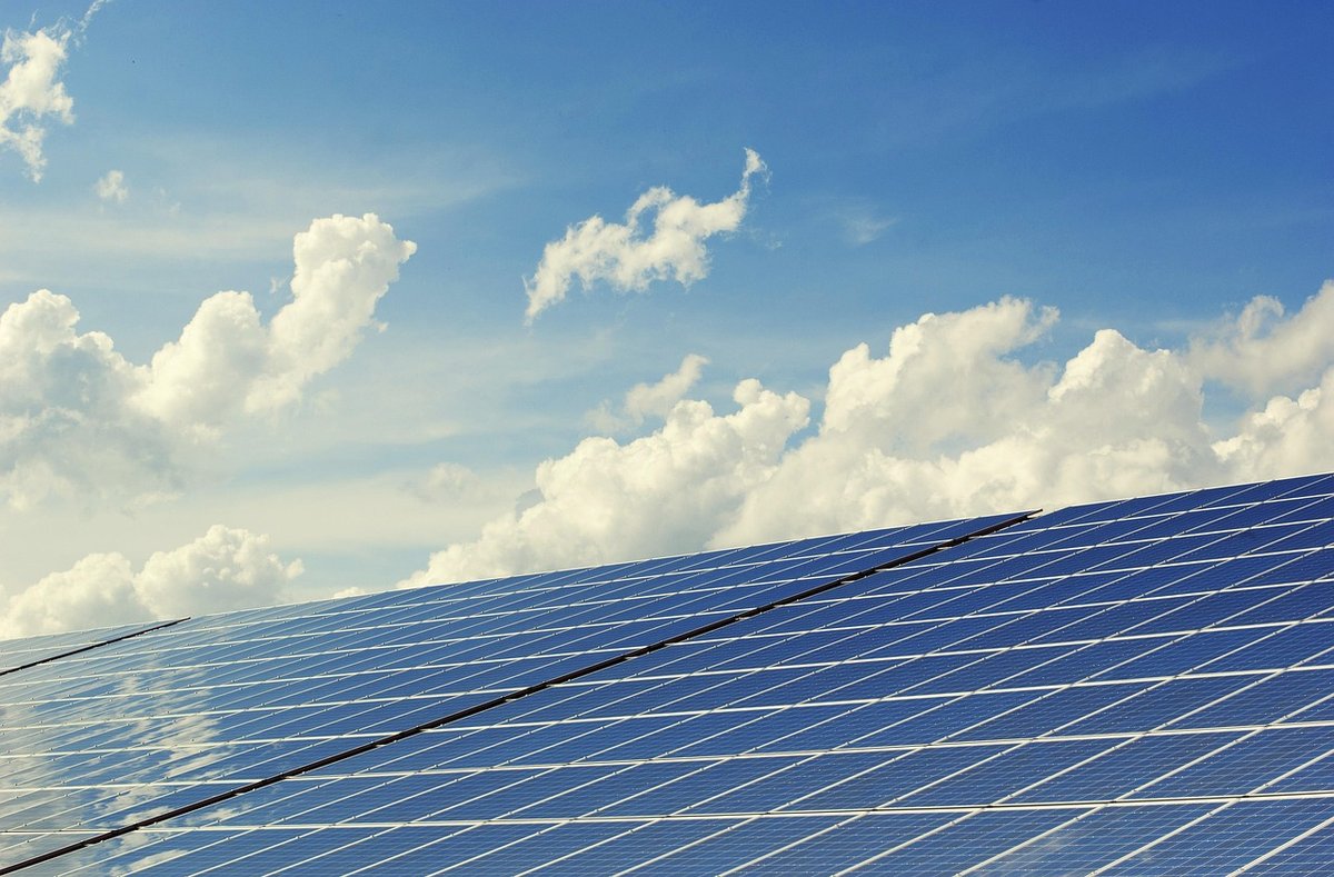 Rows of blue solar panels angled under a bright sky with white clouds